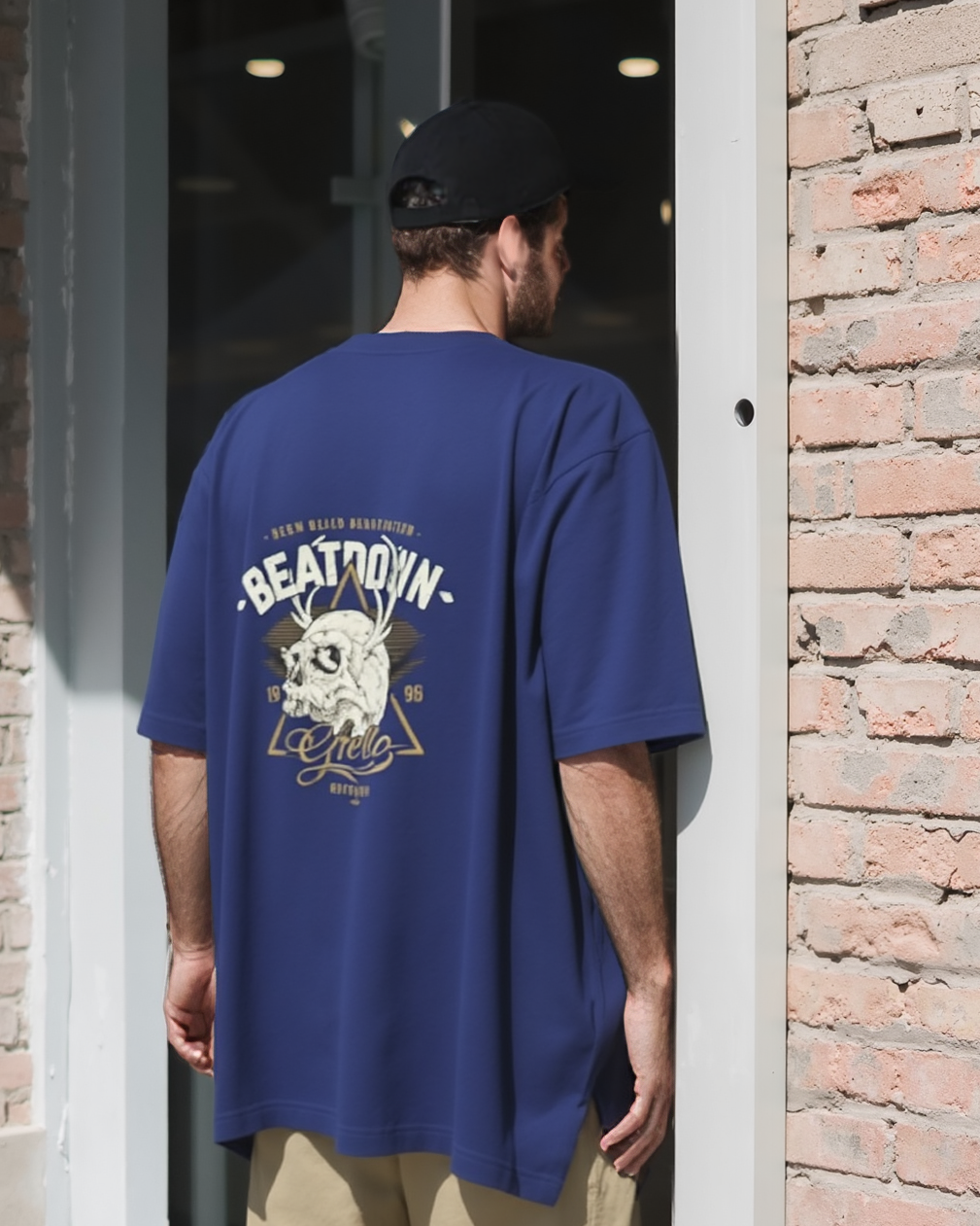 Person wearing a blue oversized t-shirt with a graphic design, standing in front of a brick wall.