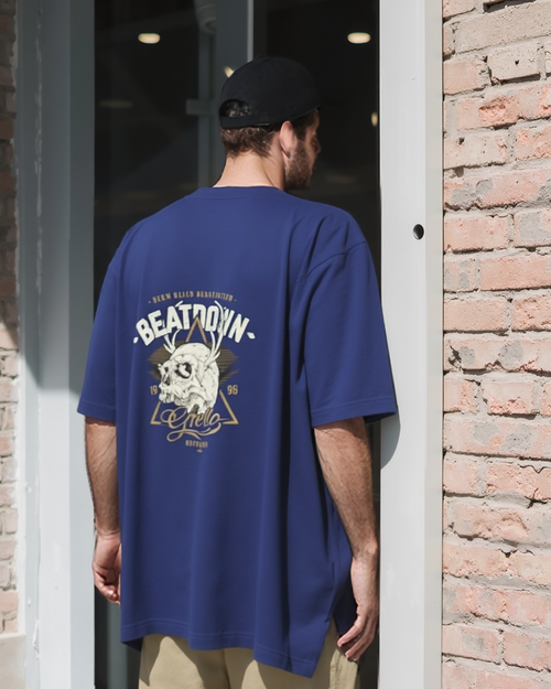 Person wearing a blue oversized t-shirt with a graphic design, standing in front of a brick wall.