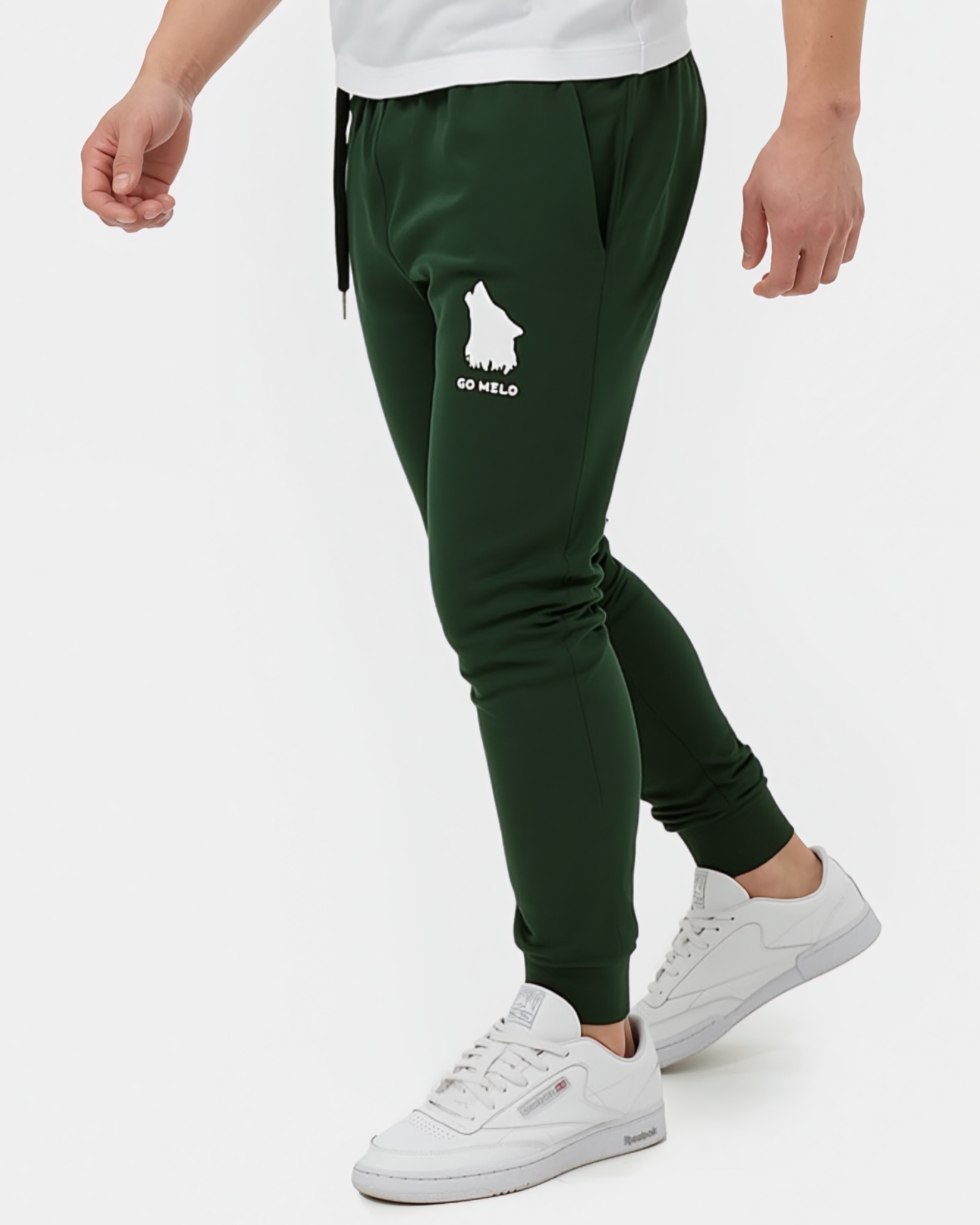 Person wearing green jogger pants with a logo and white sneakers on a white background