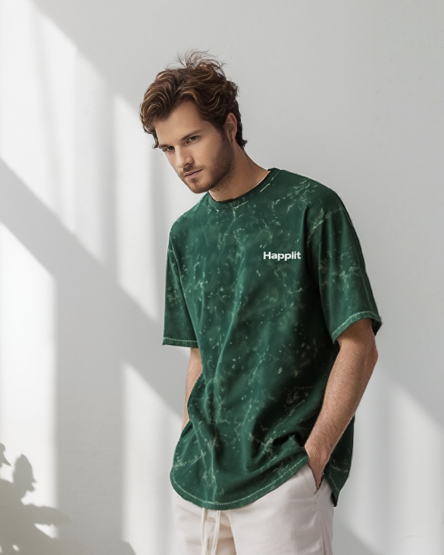 Man wearing a green t-shirt and white shorts with gold lettering, standing in a well-lit room with plants.