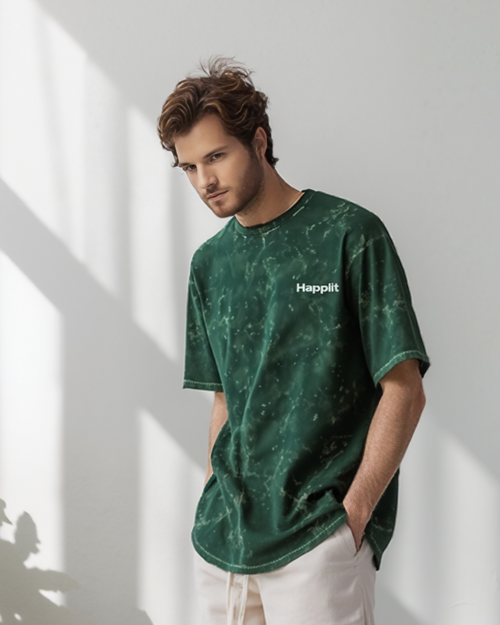 Man wearing a green t-shirt and white shorts with gold lettering, standing in a well-lit room with plants.