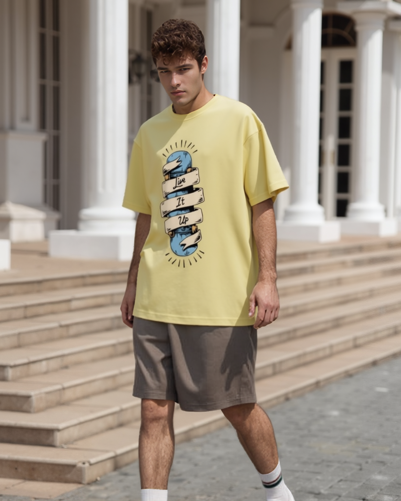 Man wearing a yellow t-shirt with a graphic design, brown shorts, and white sneakers standing in front of classical architecture.