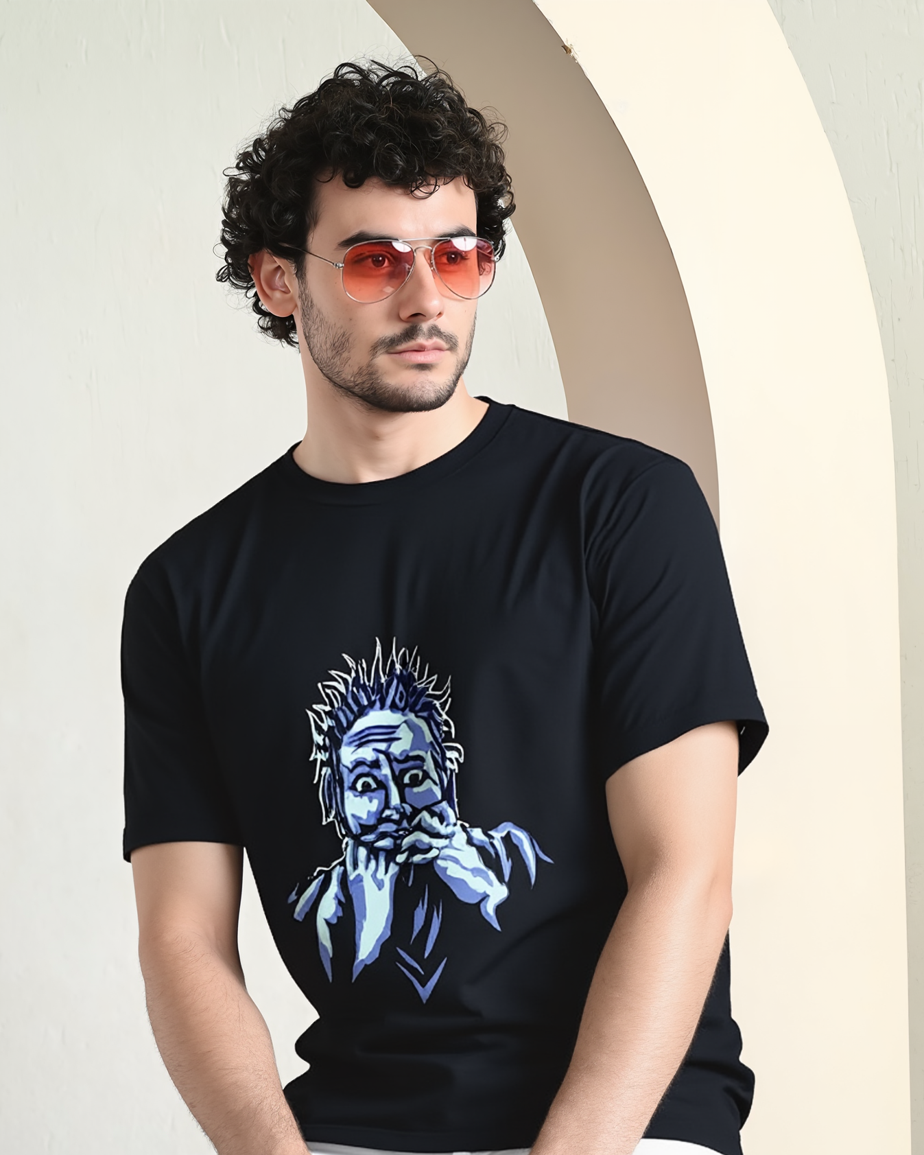 Man wearing a black t-shirt with a graphic design, sitting against a light-colored wall.