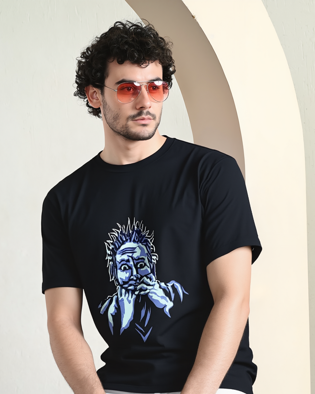 Man wearing a black t-shirt with a graphic design, sitting against a light-colored wall.