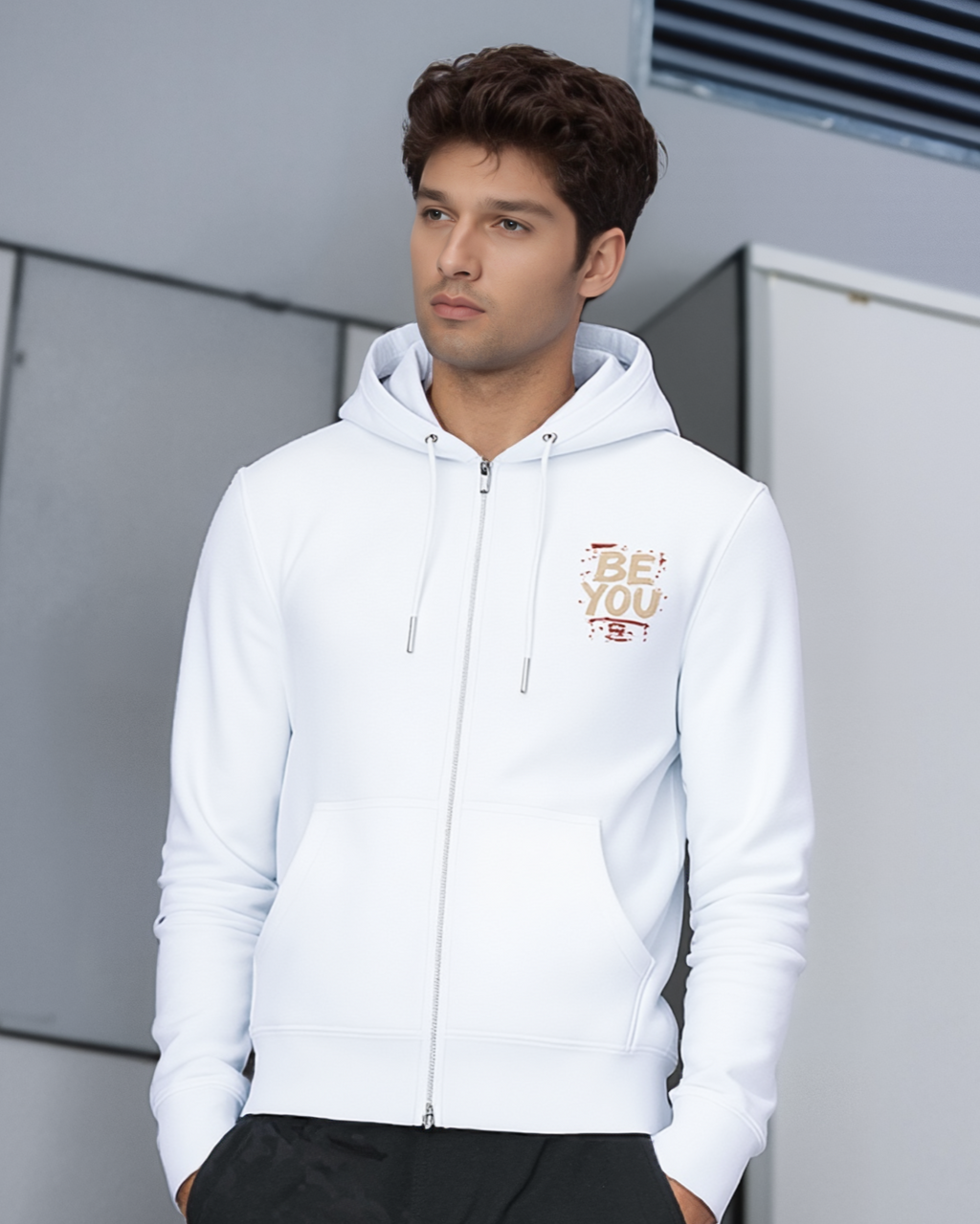 Man wearing a white hoodie with text on it, standing against a modern building exterior.
