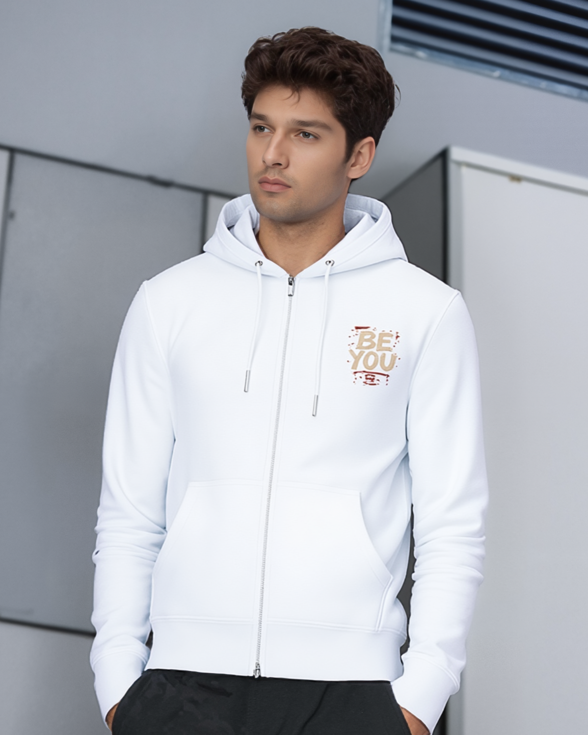 Man wearing a white hoodie with text on it, standing against a modern building exterior.